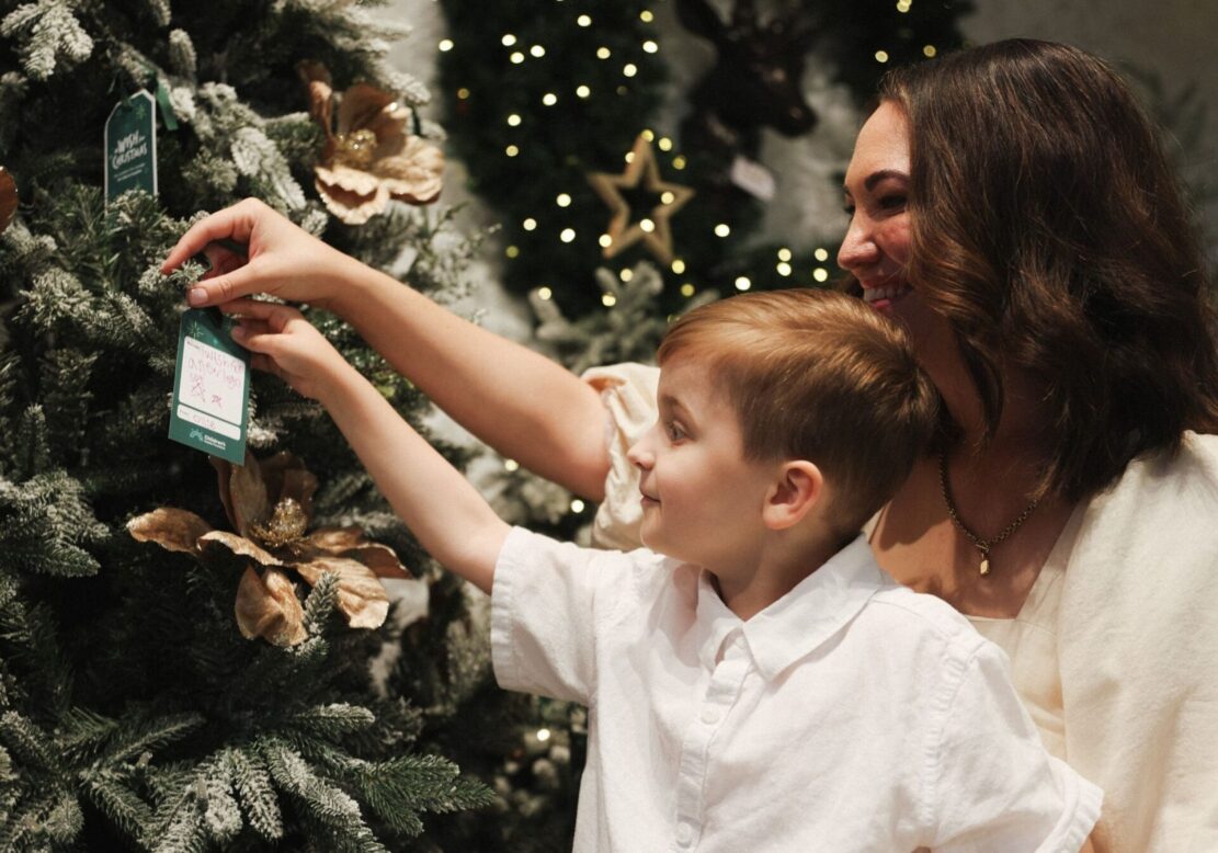 Mother and son hang Children's Hospital Foundation 'Make a Wish' tag on Christmas tree
