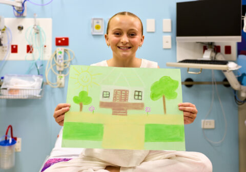 Evie, 12, cystic fibrosis, holds a drawing of her home in a hospital treatment room