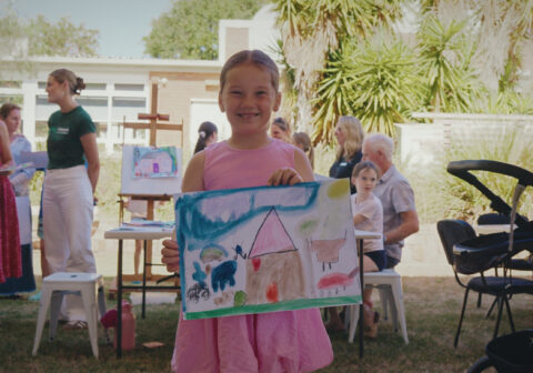 Young girl holds up drawing of home at 2026 Warwick community art workshop