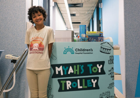 Myah stands next to the toy trolley she donated to QCH oncology ward